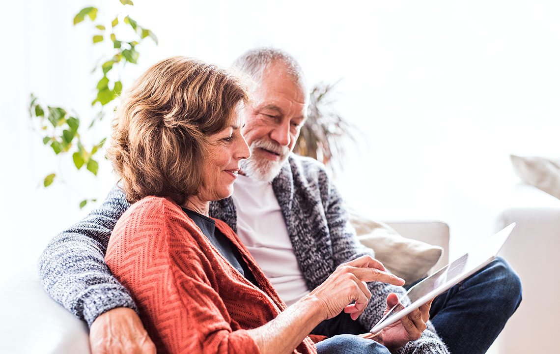 elderly couple sitting together using an iPad